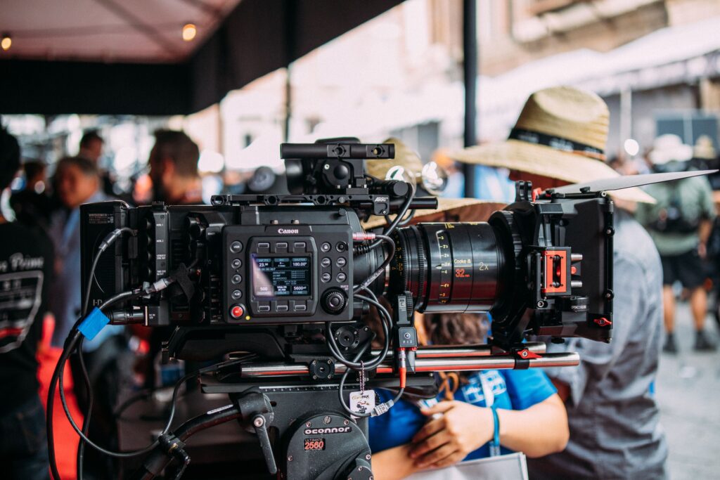 Current image: Close-up of a professional video camera setup at an outdoor event focusing on filmmaking equipment.